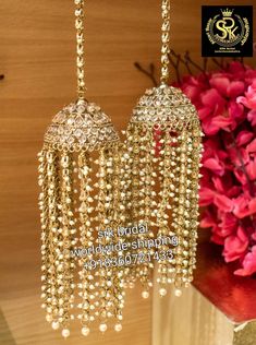 two gold colored chandeliers hanging from a wooden shelf next to flowers and vases