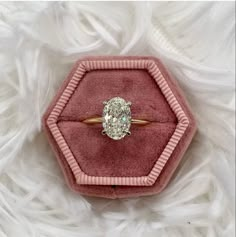 an oval shaped diamond ring in a velvet box on white furnishing with pink trim