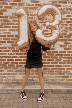 a young woman holding two large balloons in front of a brick wall with the number thirteen on it