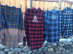 four flannel shirts are hanging on a clothes line in front of a rock wall