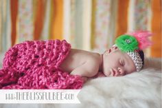 a baby sleeping on top of a bed wearing a crochet hat and pink blanket