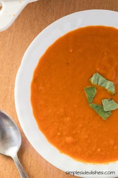 a white bowl filled with red soup and garnished with green leafy leaves