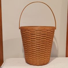 a brown basket sitting on top of a white table next to a wooden chair and wall