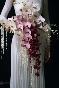 a woman in a white dress holding a bouquet of pink and white orchids with pearls