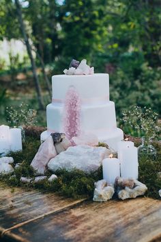 a white wedding cake with pink icing and rocks on the ground next to it