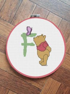 a cross stitch winnie the pooh with a purple butterfly sitting on top of it