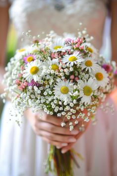 a bride holding a bouquet of daisies and baby's breath