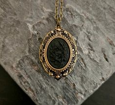 A detailed black on black rose cameo set in detailed antiqued brass, on an antiqued brass locket.  Chain is antiqued brass.  Locket opens with two spaces. Details: Locket measures 1.25 inch x 7/8 inch Chain measures 18 inches Locket and chain are plated brass Back of locket is engraved as shown Cameo is hard, matte resin Lead and nickel free Please allow for possible slight color differences due to different settings on different screens. Thank you for shopping Delicate Industry :) Black Engraved Brass Necklaces, Black Brass Medallion Jewelry, Vintage Black Locket Necklace, Black Medallion Locket Necklace As A Gift, Vintage Black Locket Jewelry, Gothic Brass Jewelry Gift, Vintage Black Locket Necklace Gift, Gothic Bronze Jewelry With Antique Finish, Bronze Gothic Jewelry For Gift