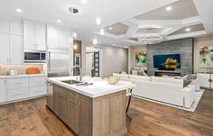 a large open concept kitchen and living room with wood flooring, white cabinets and an island