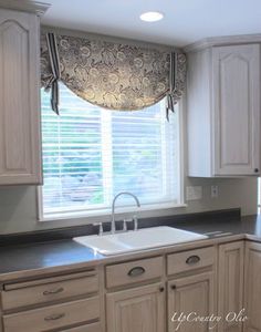 a kitchen sink under a window in front of white cabinets and cupboards with black counter tops