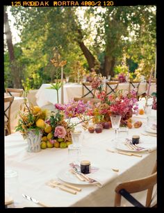 the table is set with flowers, fruit and candles for an outdoor dinner party or celebration