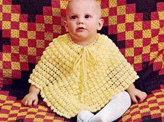 a baby wearing a yellow crochet shawl sitting on a red and yellow blanket