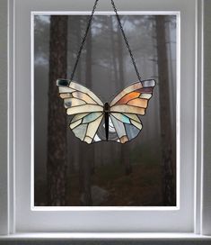 a stained glass butterfly hanging from a chain in front of a forest filled with trees