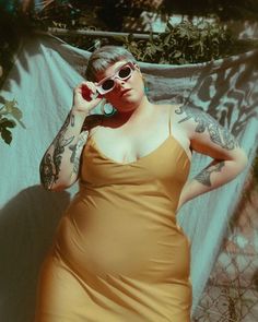 a woman in a yellow dress with tattoos on her arms and legs is talking on the phone