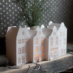 three small white houses sitting on top of a table next to a potted plant