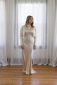 a woman standing in front of a window wearing a white dress