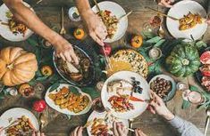 several people are eating at a table with plates and bowls on it, all holding food