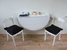 two white chairs with black cushions sit in front of a small round table and shelf