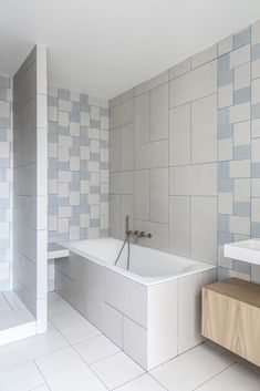 a bath tub sitting next to a white sink in a room with tiled walls and floor