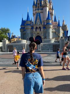 a woman standing in front of a castle with people walking around it at disney world