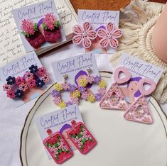 there are some pretty pink and purple earrings on the table with other items in front of them