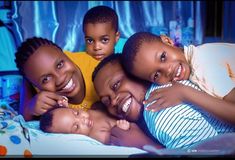 a group of children laying on top of a bed smiling at the camera with their arms around each other