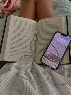 an open book sitting on top of a bed next to a cell phone and headphones