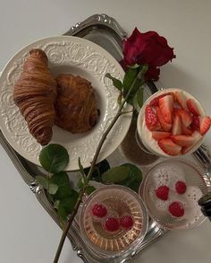 a tray topped with croissants and strawberries next to a bowl of fruit