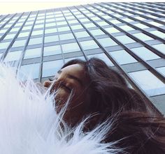 a woman with long hair standing in front of a tall building and looking up at the sky