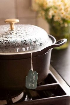 a pot on the stove with a tag hanging from it's side and flowers in the background