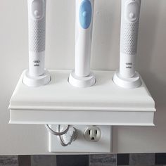 three electric toothbrushes sitting on top of a white shelf next to each other