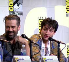 two men sitting in front of microphones at a press room table with water bottles