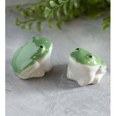 two green and white frog figurines sitting next to each other on a table