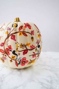 a white pumpkin decorated with multicolored flowers and leaves on a marble countertop