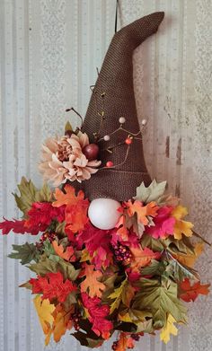 a scarecrow hat hanging on the wall with autumn leaves and an egg in it