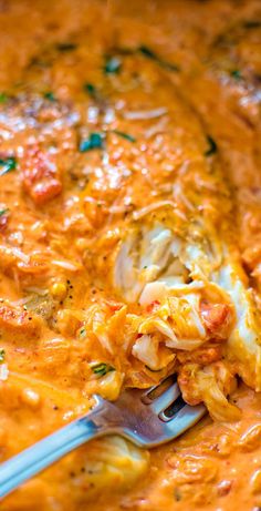 a spoon with some food in it on top of a pan filled with cheese and sauce