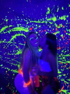 two women are kissing in front of an image of glow paint on the wall behind them