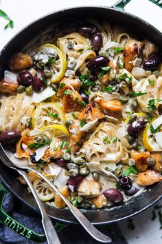 a skillet filled with pasta, olives, and chicken on top of a table