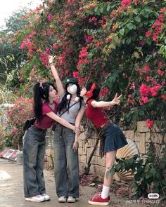 three young women standing next to each other with their arms in the air and flowers behind them