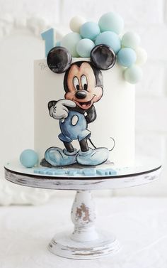 a mickey mouse birthday cake with blue and white balloons on the top, sitting on a pedestal