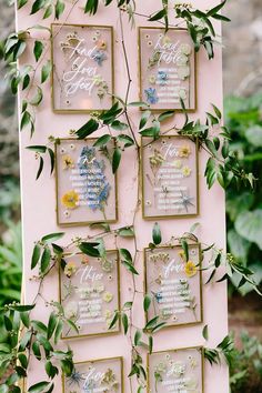 a pink and gold wedding seating chart with greenery on the sides, hanging from a wall