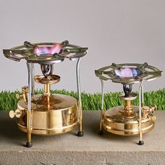 two brass candlesticks sitting on top of each other in front of green grass