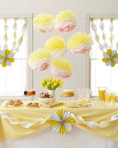 a table topped with yellow and pink paper pom poms next to two windows