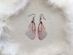 the pink and white feathers are hanging from silver earwires on a white background