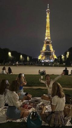 people are sitting on the grass in front of the eiffel tower at night