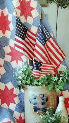 an american flag quilt and potted plant on a table with other patriotic flags in the background