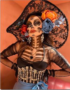 a woman with makeup painted to look like a skeleton wearing a hat and holding an orange flower in her hair