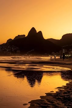 the sun is setting at the beach with mountains in the background