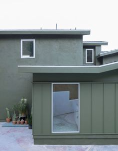 a green building with potted plants in front of it and two windows on the side