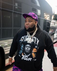 a man in a black hoodie and purple pants is standing next to a bus